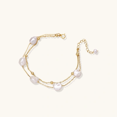 Double-strand gold bracelet with irregular baroque pearls and smooth freshwater pearls on cream background.