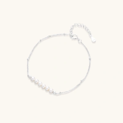 Delicate rhodium-plated silver chain bracelet with row of small baroque pearls centered on white background.