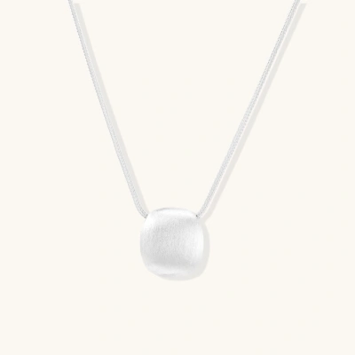 Minimalist brushed sterling silver dome pendant on delicate chain against cream background, showing matte textured finish