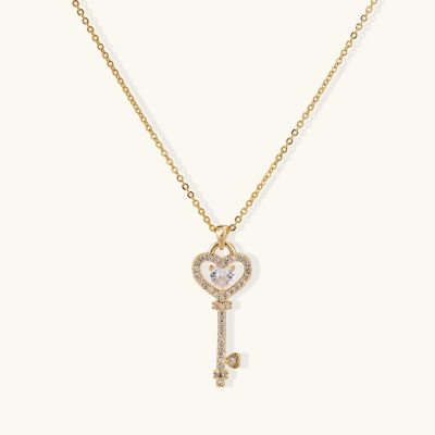 Delicate gold key pendant with heart-shaped bow and crystal pavé detailing on fine chain against cream background.