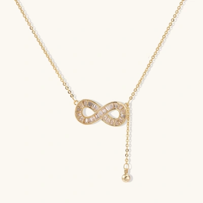 Gold infinity pendant with baguette crystals on adjustable chain against cream background.