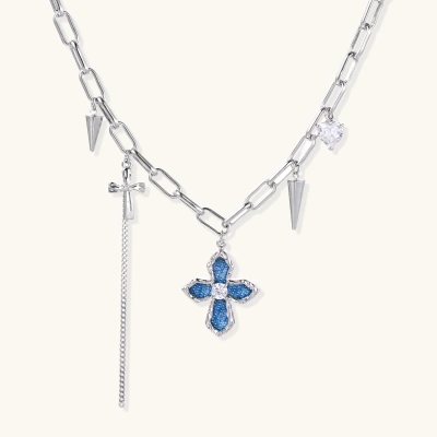 White gold plated chain necklace with blue textured cross pendant, spike charms, and mini cross detail on beige background