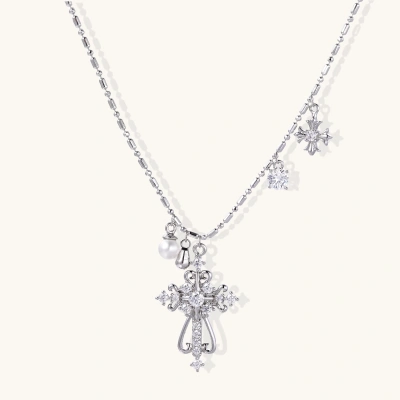 Ornate white gold-plated cross pendant with zirconia stones and pearl accents on adjustable silver chain against cream background