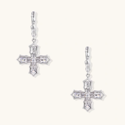 Ornate white gold-plated cross earrings with baguette-cut zirconia stones and twisted leverback hooks on beige background