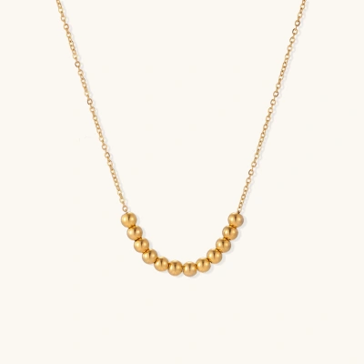 Delicate gold-plated necklace with graduated spherical beads forming gentle smile curve on beige background