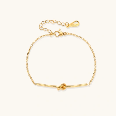 Delicate gold chain bracelet with minimalist bar and centered knot detail on cream background