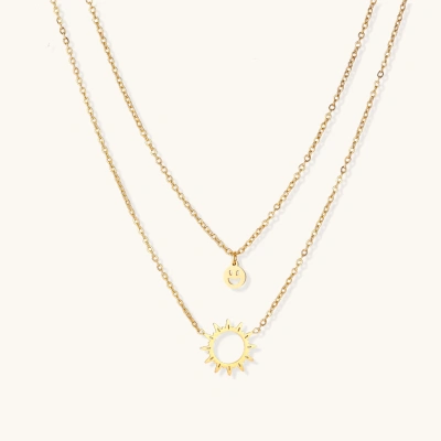 Gold layered necklace set with sunburst and smiley face pendants on delicate chains against white background.