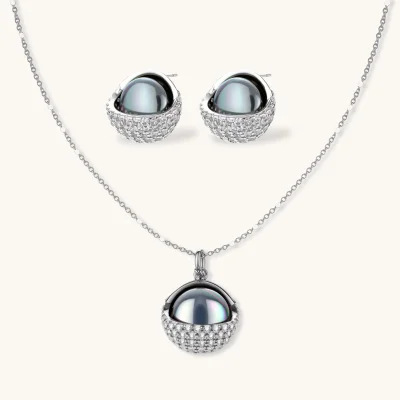 Elegant spherical pendant necklace and earrings set featuring crystal-pavé bottom half in gold or silver finish on white background.