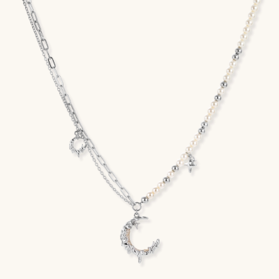 Silver-toned crescent moon pendant with star accents on pearl and chain necklace against white background.