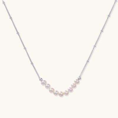 Delicate sterling silver chain necklace with small freshwater pearls arranged in a curved smile arc on cream background.