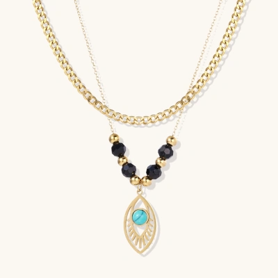 Layered gold necklace with turquoise evil eye pendant and black quartz beads on cream background