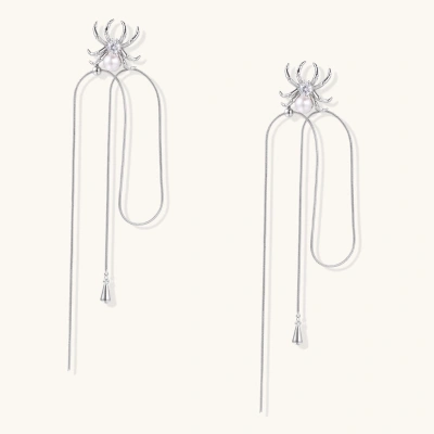 White gold plated spider earrings with pearl body and long threader chains on beige background