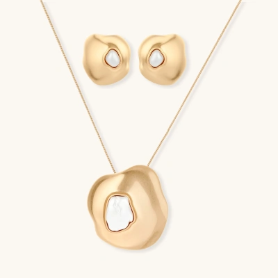 Close-up of organic gold-toned earrings and necklace with white baroque pearls on neutral background.