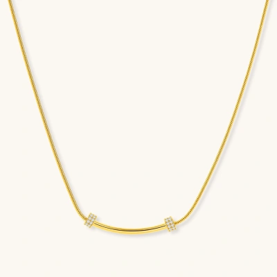 Delicate gold-plated necklace with curved bar pendant and crystal accents on snake chain against cream background.