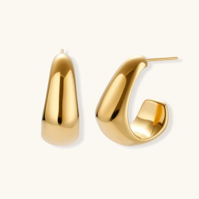 Close-up of curved gold-plated huggie earrings with sculptural design on white background, showing polished finish.
