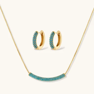 Gold-plated curved necklace and hoop earrings with turquoise cubic zirconia stones on white background.