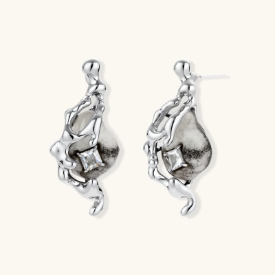Sculptural silver drop earrings with flowing metal curves around marbled resin stones and crystal accents on white background.