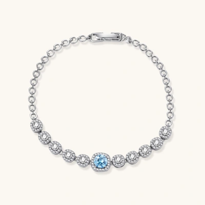 Sterling silver tennis bracelet with round halo-set moissanite stones and blue center stone on cream background.