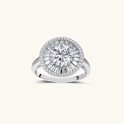 Brilliant round moissanite center stone with baguette and round halo accents in sterling silver setting on light background.