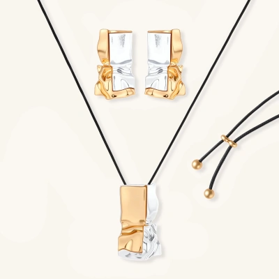 Modern jewelry set with abstract gold and silver pendant on black cord necklace plus matching geometric earrings on white background.