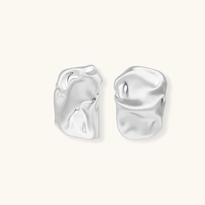 Pair of sculptural silver ear cuffs with organic fluid shapes and polished finish against cream background.