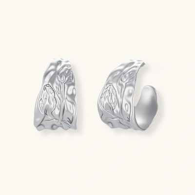 Close-up of textured silver hoop earrings with embossed floral pattern and sterling silver posts on cream background