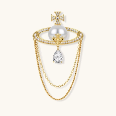 Ornate gold-plated cross brooch with central pearl, zirconia crystals, and draped chain details on neutral background.