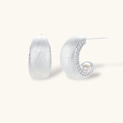Close-up of small silver-plated hoop earrings with brushed texture and a row of sparkling zircon crystals on white background
