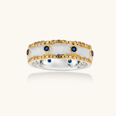 Close-up of ornate two-tone gold plated ring with blue zirconia stones in decorative circular settings on neutral background.