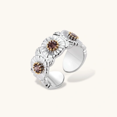 Close-up of adjustable copper ring with three dimensional flowers, dark zircon centers and gold-plated details on cream background.