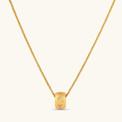 Gold-plated cylindrical ring pendant with brushed finish and scattered crystal accents on a wheat-link chain, cream background.