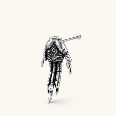 Silver stainless steel stud earring shaped like a skeletal demon claw hand with an eye motif on the palm and sharp talon fingers.
