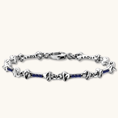Sterling silver bone-link bracelet with blue cubic zirconia stones and engraved motifs, lobster clasp, on cream background.