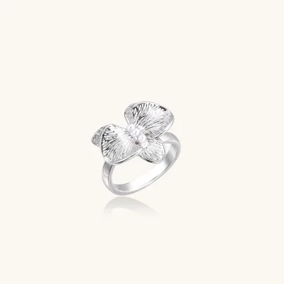 White gold plated eco-brass orchid ring with textured petals, sparkling zirconia accents and three white beads on a cream background.