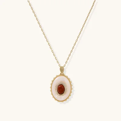 Gold plated eco-brass necklace with an oval white pendant, a central red-brown stone and a zirconia halo on a cream background.