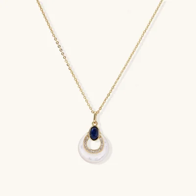 Gold plated chain necklace with a white MOP crescent pendant, blue lapis lazuli oval and sparkling stone accents on a cream background.