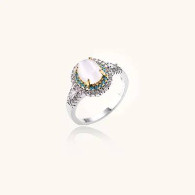 White gold plated eco-brass halo ring with an oval milky cat's eye stone, teal beads and clear crystals on a cream background.