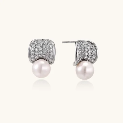 Pair of white gold plated eco-brass stud earrings with curved sparkling stone panels and round freshwater pearls on a cream background.