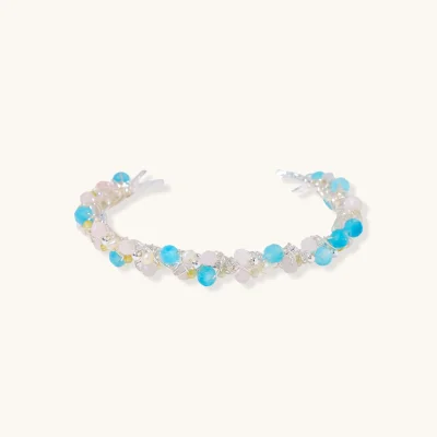 Open wire-wrapped cuff bracelet with aqua blue, blush pink and pale yellow beads and freshwater pearls on a cream background.