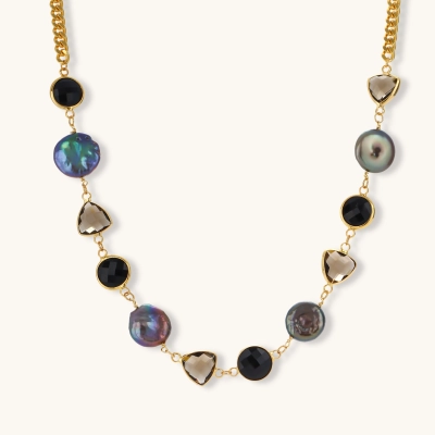 Gold plated curb chain necklace with iridescent baroque pearls, black round stones and smoky triangular stones on a cream background.