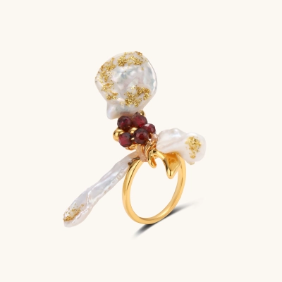 Gold plated adjustable ring with three gold-flecked baroque pearls and a cluster of deep red faceted beads on a cream background.