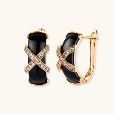 Pair of gold plated black ceramic huggie earrings with a zircon-studded X motif and latch-back closure on a cream background.
