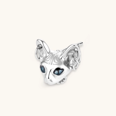 Single silver plated eco-brass stud shaped like a hairless cat head with blue CZ eyes and tiny hoop piercings on a cream background.