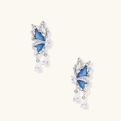 Silver butterfly earrings with blue denim fabric wings and dangling teardrop crystals on cream background