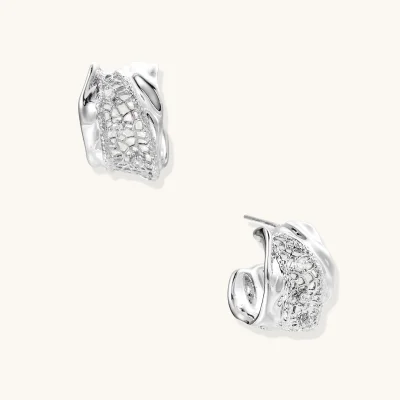 Close-up of sculptural hoop earrings with lattice center band and smooth twisted edges in white gold-plated brass with zirconia