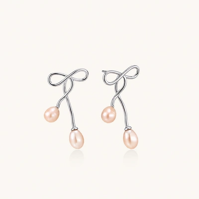 Rhodium-plated silver earrings with organic vine curves and two peachy freshwater pearls on cream background