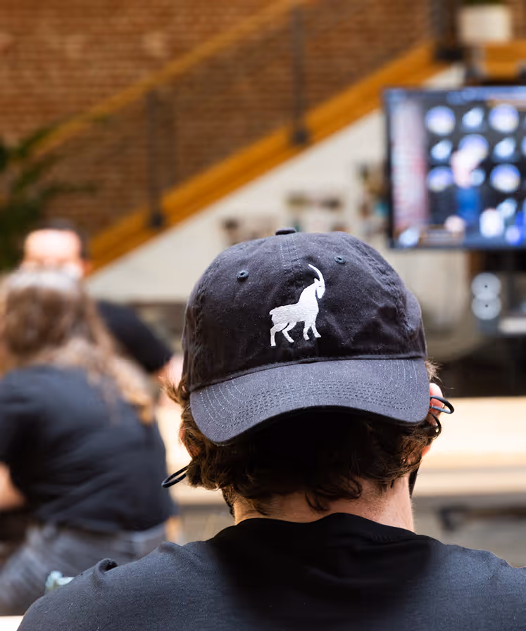 Capella team member facing away from camera wearing a Capella ball cap with the Capella goat in white 
