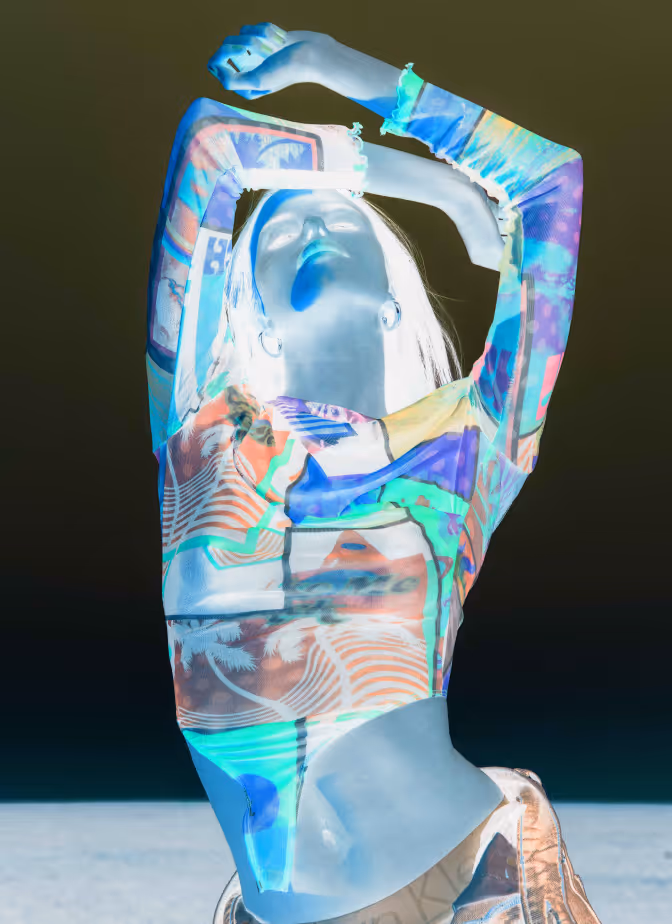 Woman posing with arms raised above head wearing a colorful patterned long-sleeve top.