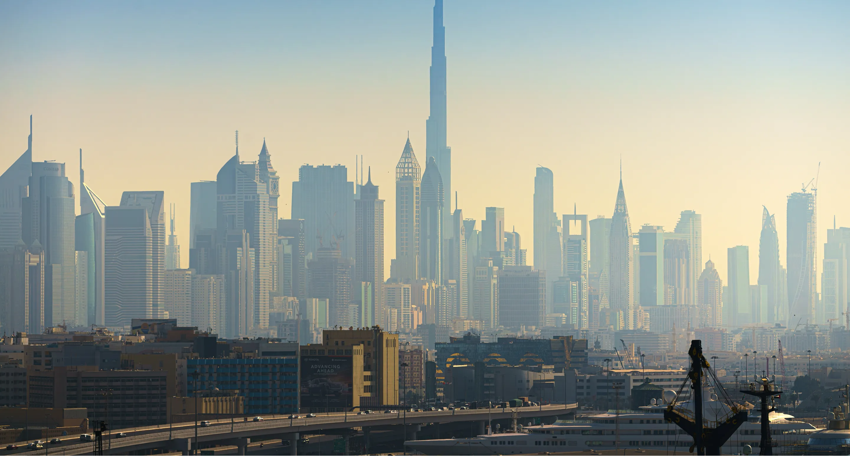 Panoramic view of a modern city skyline with numerous high-rise buildings under a clear sky at dawn or dusk.