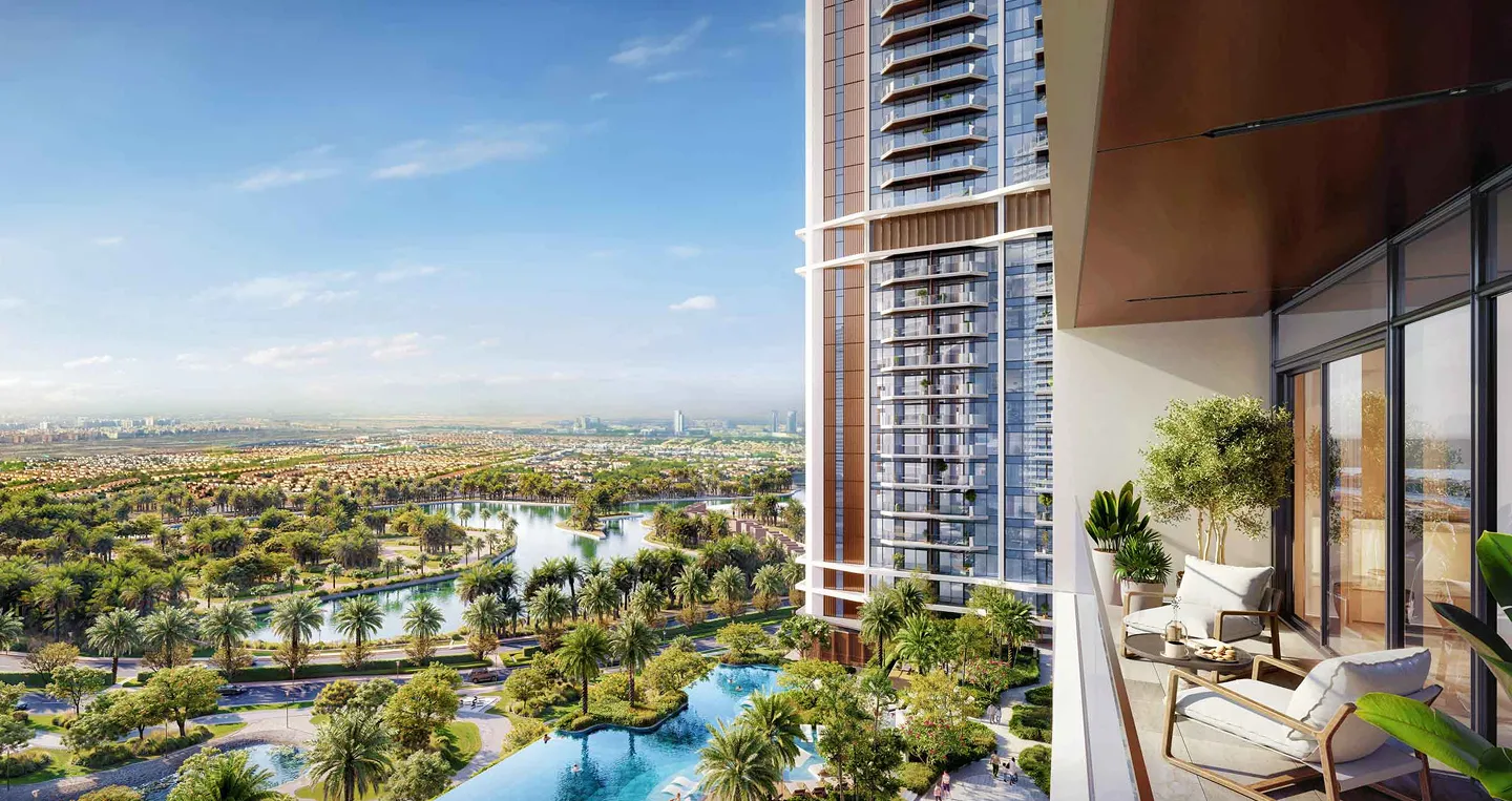 View from a modern apartment balcony overlooking a landscaped garden with a water feature and palm trees, extending to a cityscape under a blue sky.